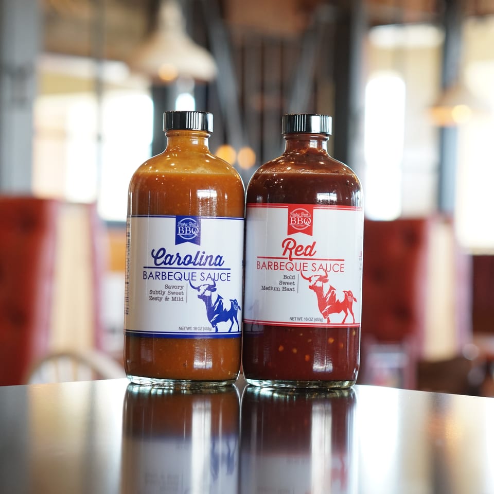Two Ruby Red’s BBQ bottles, Carolina and Red barbecue sauces, stand on a reflective restaurant counter.