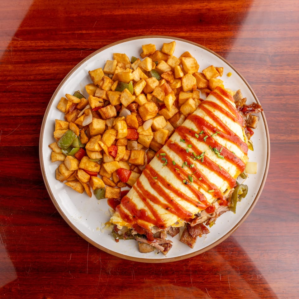 Plate of diced roasted potatoes, peppers, onions, and sliced grilled chicken drizzled with red sauce and garnished with chives.