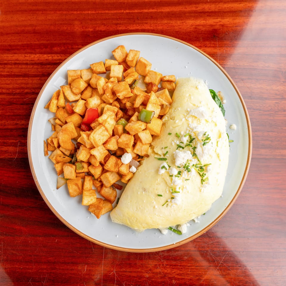 Overhead view of a cheese-filled omelet topped with chives beside golden diced potatoes and sautéed peppers.