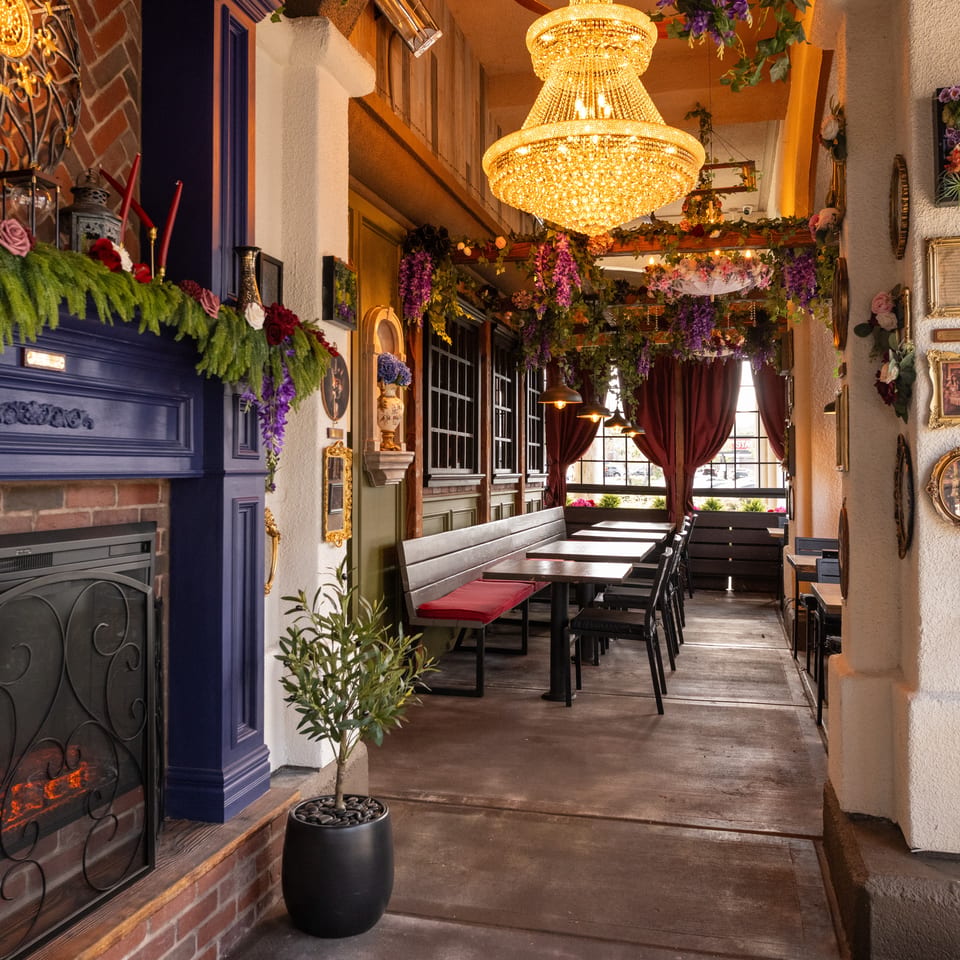 Elegant restaurant interior with floral garlands, crystal chandelier, fireplace, framed artwork, and neatly arranged tables.