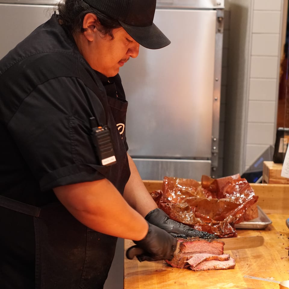Restaurant chef in black uniform slices roasted meat on a wooden cutting board in a commercial kitchen.