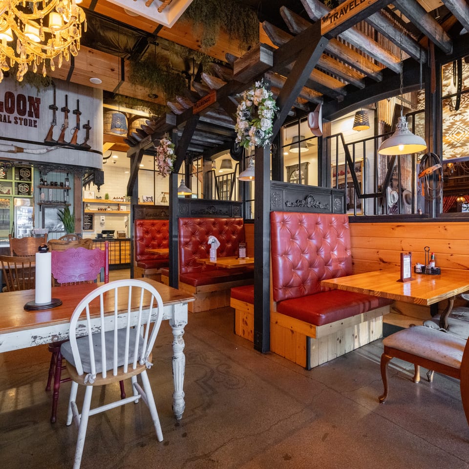 Rustic Saloon & General Store restaurant interior with red leather booths, wooden tables, chandeliers, exposed beams, and Western decor.