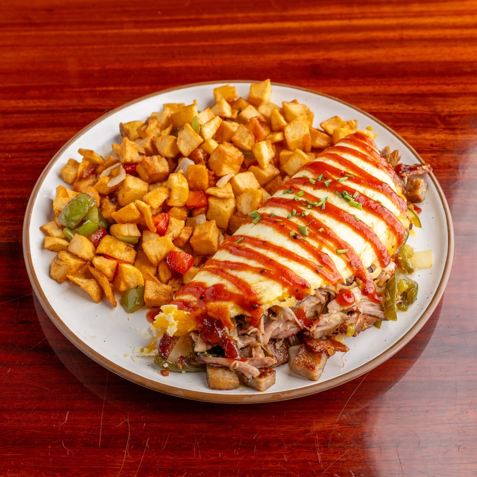 Plate of roasted potatoes, peppers, and shredded meat topped with sliced cheese, red sauce, and chives on a wooden table.