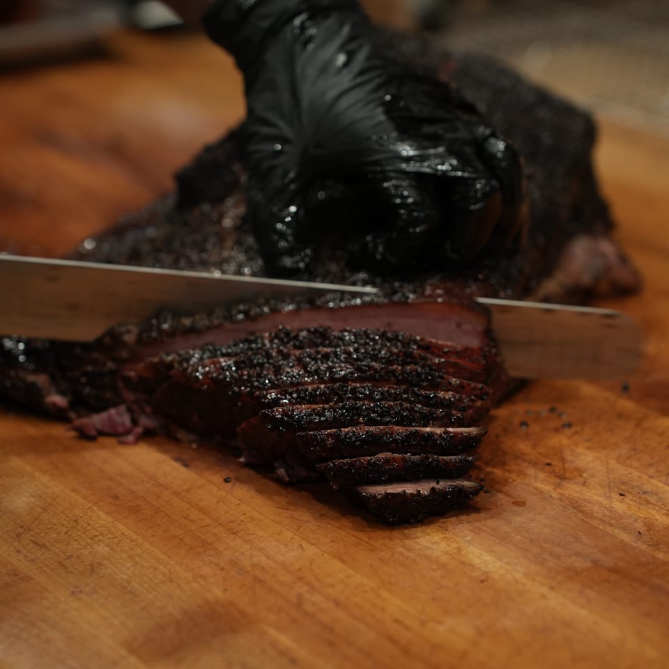 Chef slices a dark, crispy-skinned roasted duck breast on a wooden cutting board.