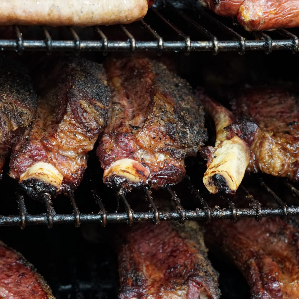 Grilled sausages and seasoned meat skewers cook on a barbecue grill.