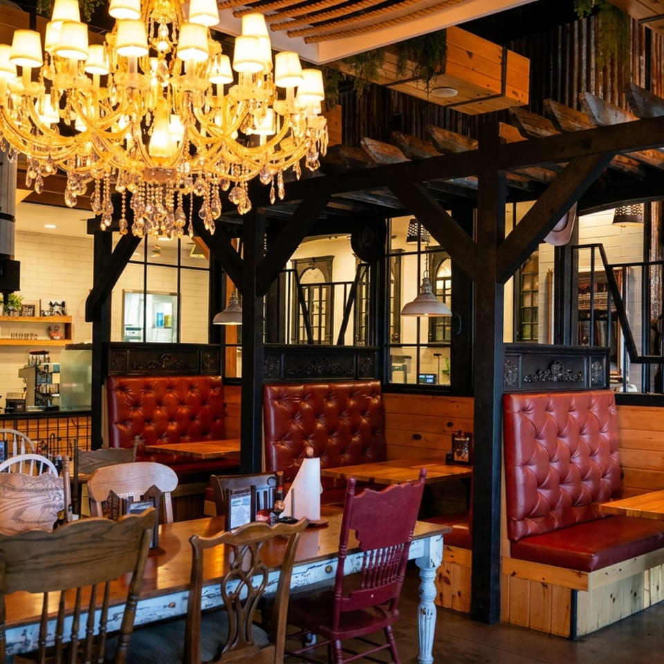 Rustic restaurant interior with red leather booths, wooden tables, industrial beams, and an ornate crystal chandelier.