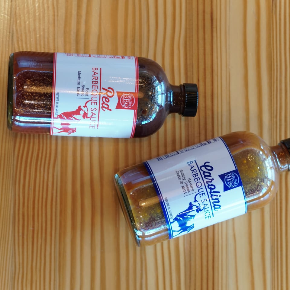 Two bottles of Carolina barbecue sauce, one bold and one original, displayed on a wooden tabletop.